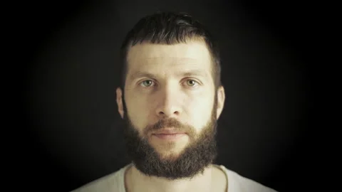 Man without emotion looks at the camera. Close up of the room on a black Stock Footage 142721619