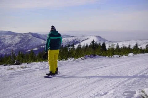 A man without a helmet in warm bright clothes goes snowboarding against the b Stock Photos