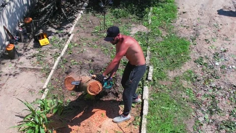 Man without t-shirt is cutting broken tree under the sun Stock Footage 156228208