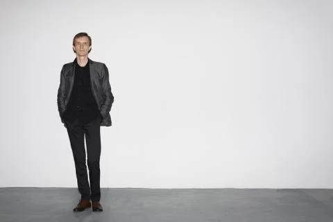 Man in wool jacket standing near white concrete wall with hands in pocket Foto stock