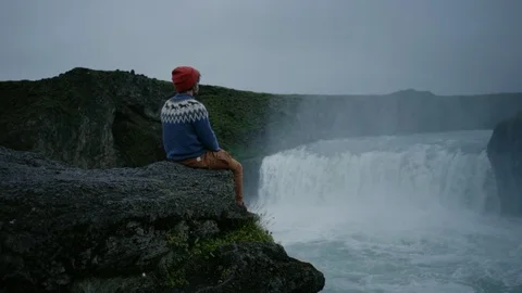 Man in wool sweater on edge of waterfall rock Stock Footage 117414787