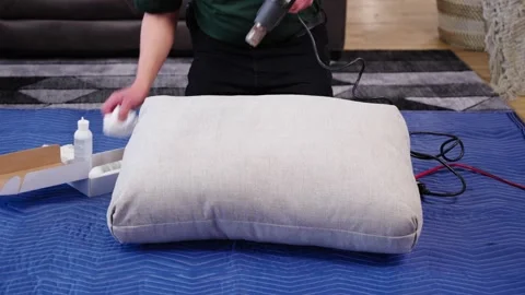 Man in Work Clothes Uses Heat Gun to Dry and Wipe Fabric Pillow on Blue Blanket Stock Footage 307823557