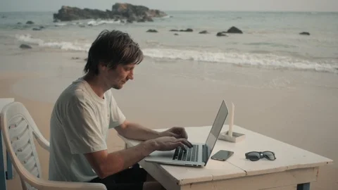 Man work on computer at the beach at sunset, freelancer programmer designer ICO Stock Footage 85611012