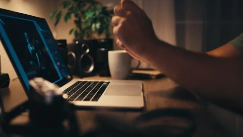 Man work on computer at night pauses with hot drink nearby while editing ph.. Stock Footage 347723466