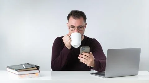 A man at work drinks coffee and looks at a smartphone Stock Photos