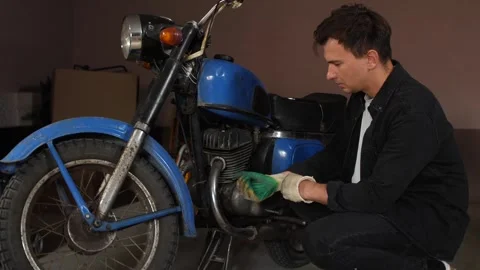 Man in work gloves inspecting and repairing a classic blue motorcycle engine Stock Footage 342762807
