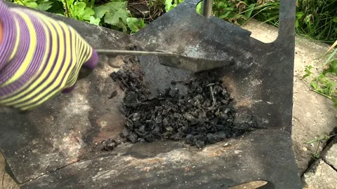 A man in work gloves scoops up coal from a barbecue outside in nature. Stock Footage 196889416