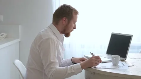A man work at home behind a laptop by a bright window 스톡 동영상 140655306