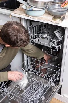 A man is at work in the kitchen, pouring salt into a dishwasher as he prepa.. Foto stock