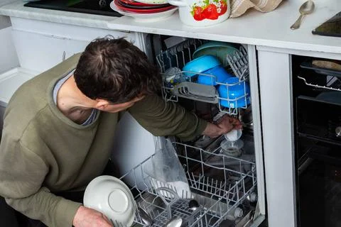 A man is at work in the kitchen, pouring salt into a dishwasher as he prepare Stock Photos