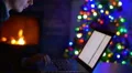 The man work with laptop - type text. By fireplace and tree New Year background 4k or 4k+ Resolution