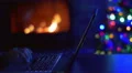 The man work with laptop - type text. By fireplace and tree New Year background 4k or 4k+ Resolution