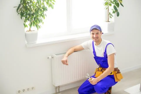 Man in work overalls using wrench while installing heating radiator in room Stock Photos