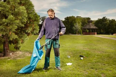 Man at work pick up garbage on grass in park Stock Photos