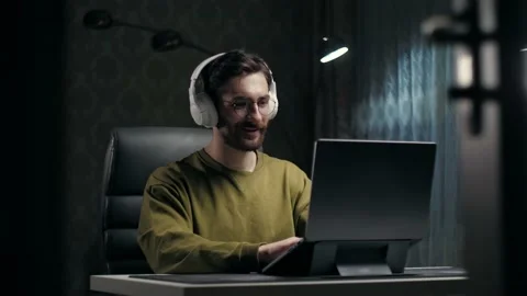 Man work remotely sitting at desk in home interior.Young guy wear headphones Stock Footage 232134420