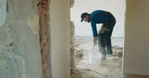 A man in a work suit with a baseball cap cleans up in an apartment under Stock Footage 219715179