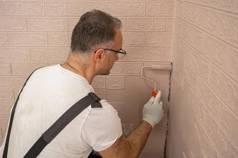 Man in a work suit paints a wall with a small roller Stock Photos