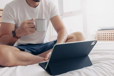 Man work with tablet and coffee in bedroom. Concept of work from home. Stock-Fotos