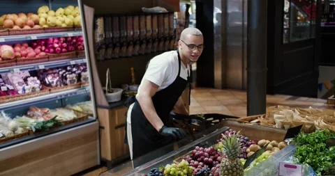 Man worker in black apron and gloves stocking the fruits in supermarket Stock Footage 235348442