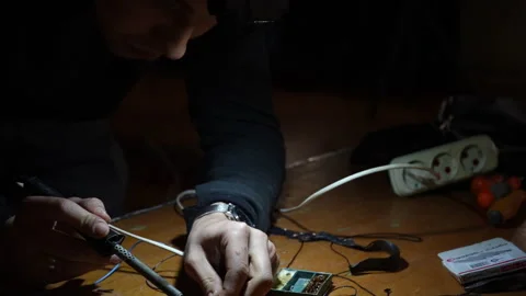 A man worker in the dark using a soldering iron connects the part to the wire Stock Footage 241718026