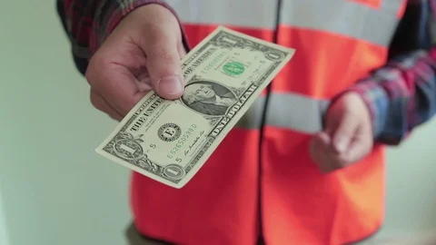 Man worker dressed in a reflective vest gives one dollar bank note to the camera Video stock 107220033