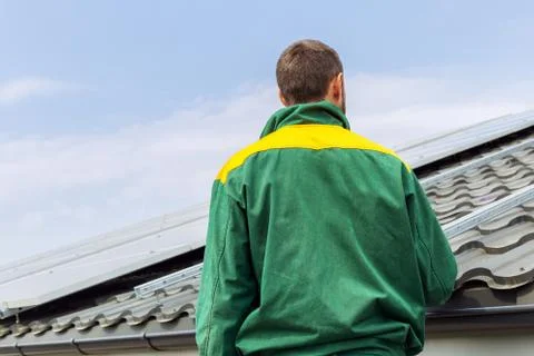 Man worker engineer against solar panels station on house roof. Back view Stock Photos