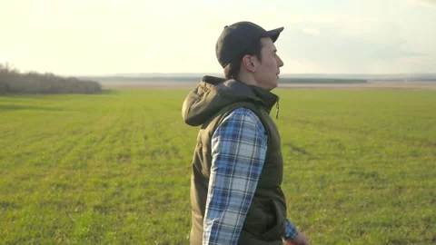 Man worker farmer red a neck in cap is walking a on green field. spring harvest Stock Footage 136460301