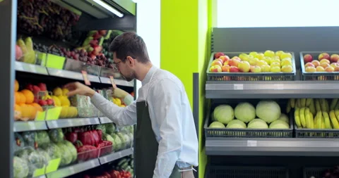 Man worker in green apron stocking the lemons in supermarket. Young employee at Stock Footage 189830244