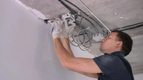 Man worker in jumpsuit puts power wires into circuit box Stock Footage 151987649
