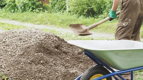 A man, a worker, loads sand and gravel mixtures into a garden wheelbarrow for Stock Footage 288177930