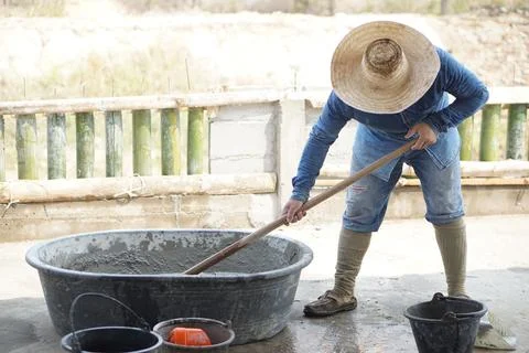Man worker manually works at construction site, using a hoe to mix cement powder Stock Photos