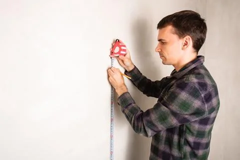 Man worker measuring and marking distance on white wall with measure tape tool Stock Photos