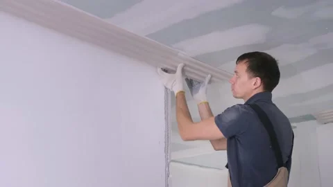 Man worker puts decorative cornice fretwork on ceiling Stock Footage 151784533