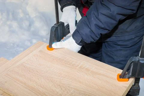 A man, a worker, secures the chipboard panels with two clamps. Stock Photos