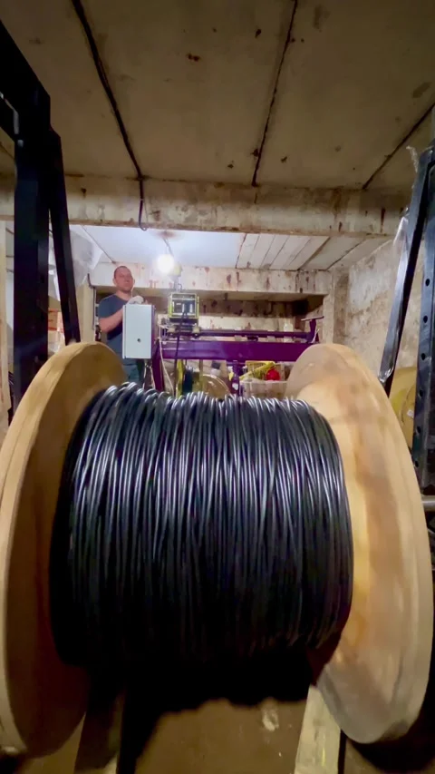 Man worker stands near machine and large wooden reel with black cable. Stock Footage 322002908