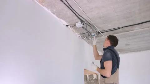 Man worker in tracksuit installs electrical junction box Stock Footage 152850163