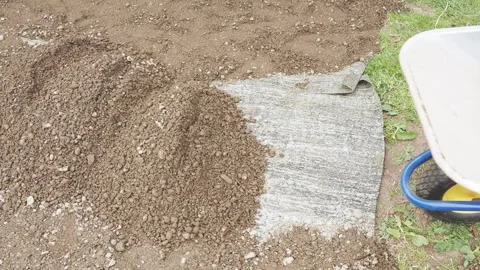 A man, a worker, unloads sand and gravel mix from a garden wheelbarrow for co Stock Footage 288178052
