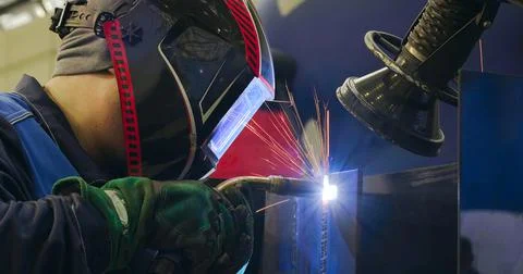 A man worker welding the seams between the metal beams indoors Foto stock