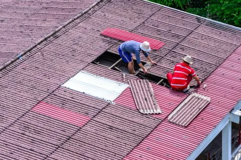 Man workers replacing damaged old tiles roof. Stock Photos