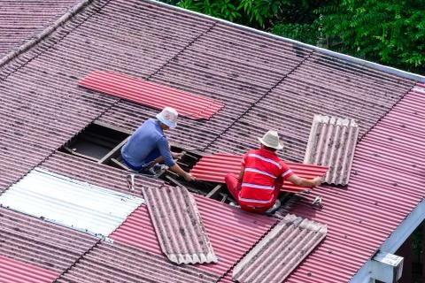 Man workers replacing damaged old tiles roof. Stock Photos