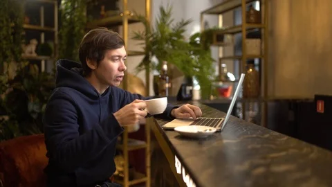 Man working on a aptop in cafe. Young freelancer is sitting in cafeteria with a Stock Footage 118964339