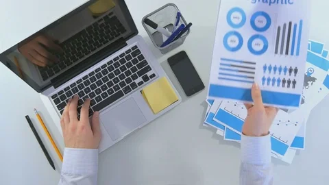 Man is working behind a laptop, he is brought papers and he sweeps them to the 库存影片 81484219