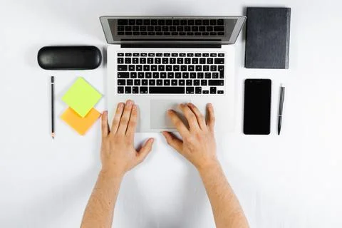 A man is working behind a laptop, a worker, a white table top view, flat lay. Stock Photos