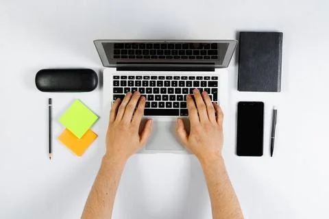 A man is working behind a laptop, a worker, a white table top view, flat lay. Stock Photos