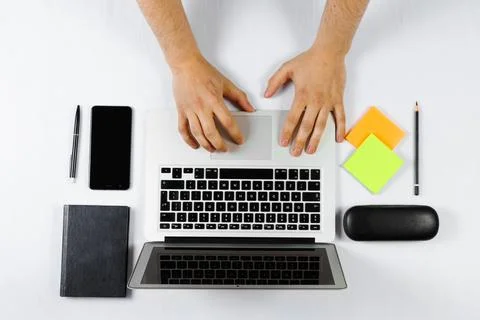 A man is working behind a laptop, a worker, a white table top view, flat lay. Stock Photos