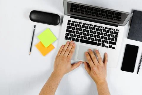 A man is working behind a laptop, a worker, a white table top view, flat lay. Stock Photos