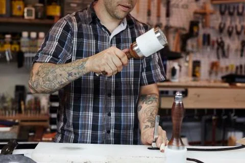 A man working at a bench in a leather workshop, using a mallet and chisel to Stock Photos