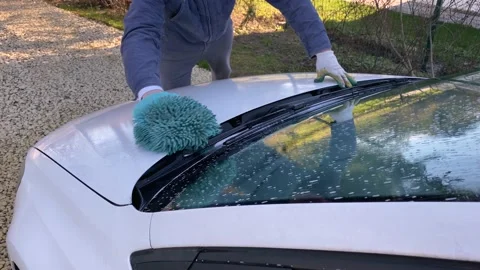 Man in working blue clothes washes a white car. he rubs the foam with a special  Stock Footage 130791909
