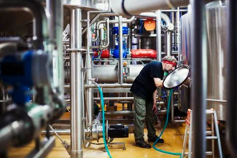 Man working in a brewery adjusting and checking the machinery which transfers Stock Photos