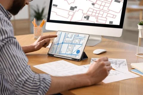 Man working with cadastral map on tablet and computer at table in office, c.. Foto stock